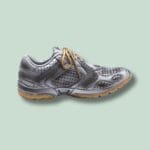 Metallisk sneaker med snørebånd på grøn baggrund.