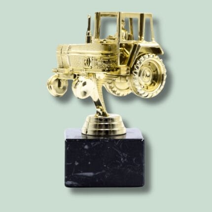 Gylden traktor statuette på sort sokkel, grøn baggrund.