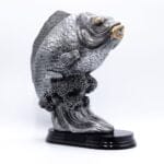 Metalfisk statue med gyldne detaljer på sort base.