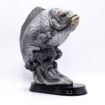 Metalfisk statue med gyldne detaljer på sort base.