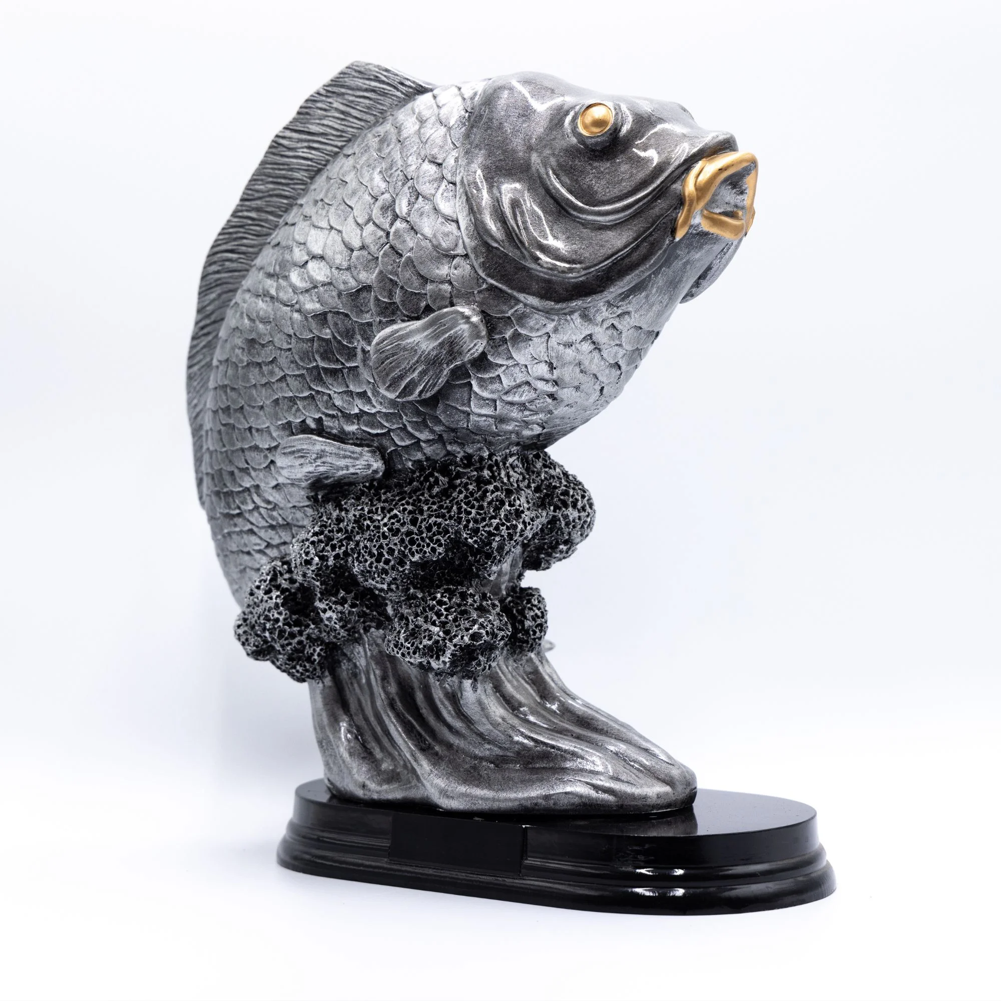 Metalfisk statue med gyldne detaljer på sort base.