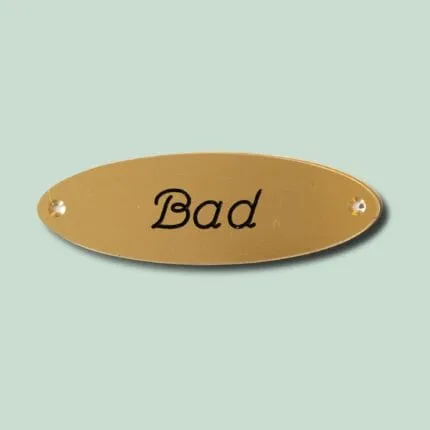 Messingskilt med teksten 'Bad' i sort skrift.