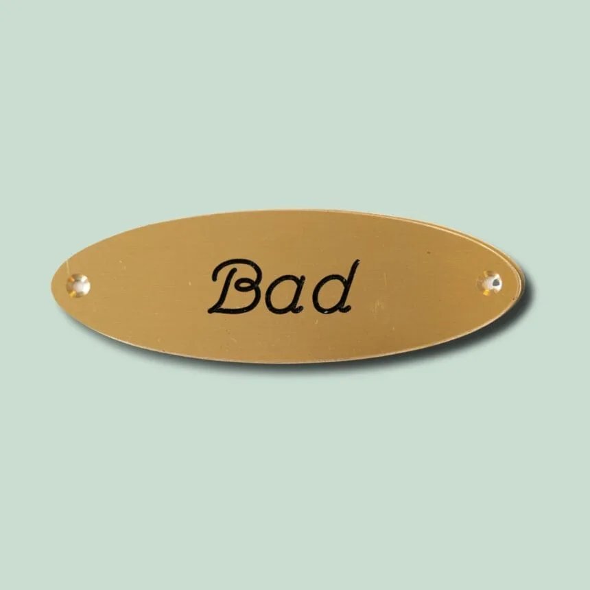 Messingskilt med teksten 'Bad' i sort skrift.