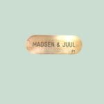 Messingskilt med tekst 'MADSEN & JUUL' på grøn baggrund.