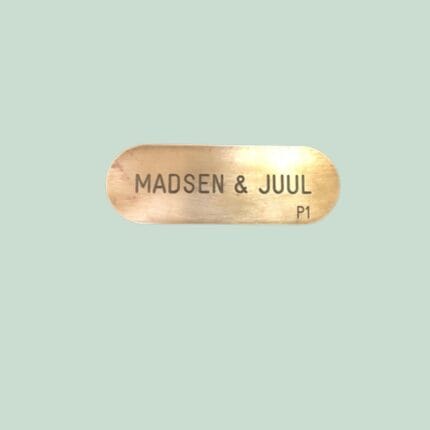 Messingskilt med tekst 'MADSEN & JUUL' på grøn baggrund.