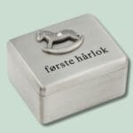 Metalæske med tekst 'første hårlok' og hestemotiv.