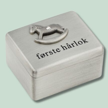 Metalæske med tekst 'første hårlok' og hestemotiv.