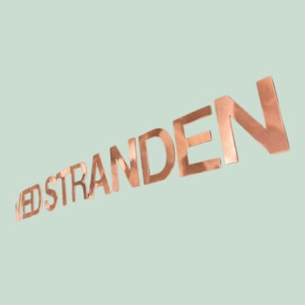 Kobbertekst 'VED STRANDEN' på lys baggrund