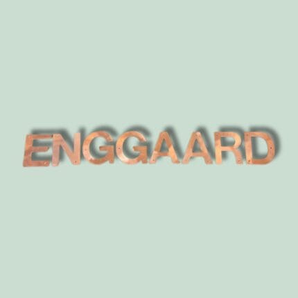 Kobberbogstaver danner ordet 'ENGGAARD' på mintgrøn baggrund.