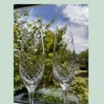 Indgraverede champagneglas foran grøn natur.
