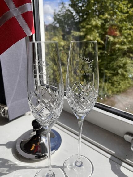 Graverede champagneglas og dansk flag ved vinduet.