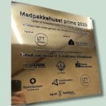 Guldplade med tekst om Madpakkehuset primo 2025.
