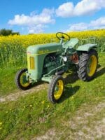 Grøn traktor på mark med gul raps