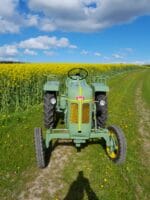 Grøn traktor på mark med rapsblomster.