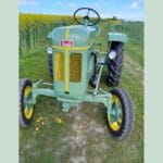 Vintage grøn traktor på en grusvej i marken.