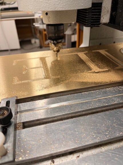 Maskine graverer tekst på metalplade i værksted.