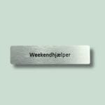 Navneskilt med teksten 'Weekendhjælper' i sort skrift.